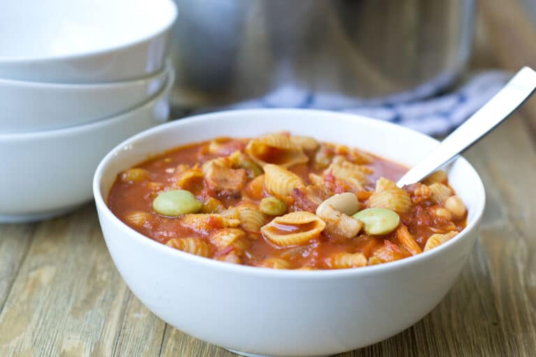 White bowl of pasta e fagioli soup with spoon.