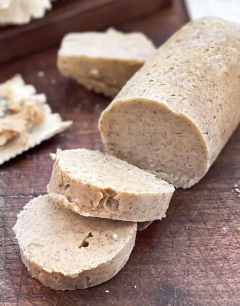 Log of pumpkin spice butter with slices cut. Some butter spread on a cracker, knife shown.