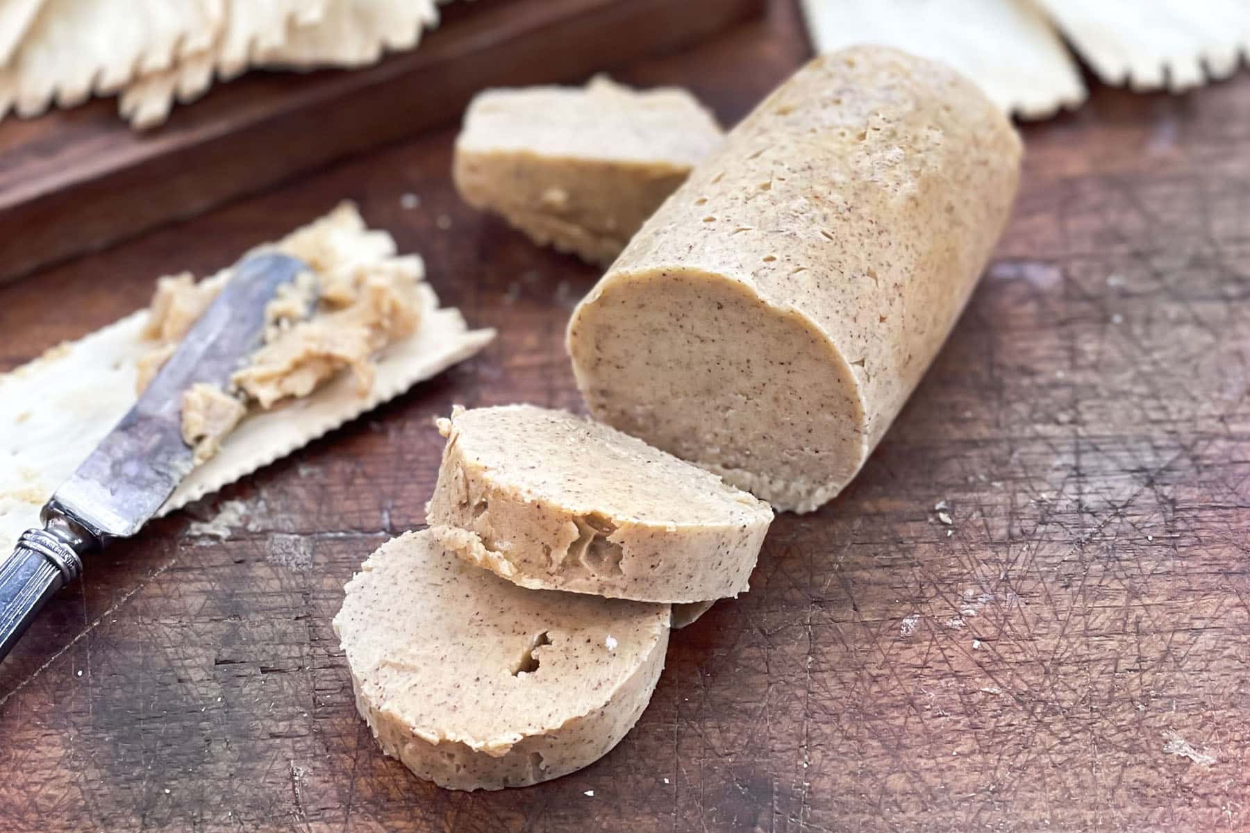 Log of pumpkin spice butter with slices cut. Some butter spread on a cracker, knife shown.