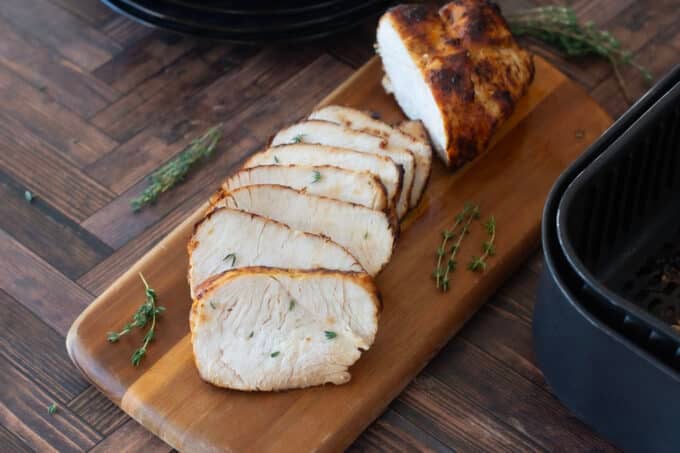 Turkey breast with slices cut on wooden board.